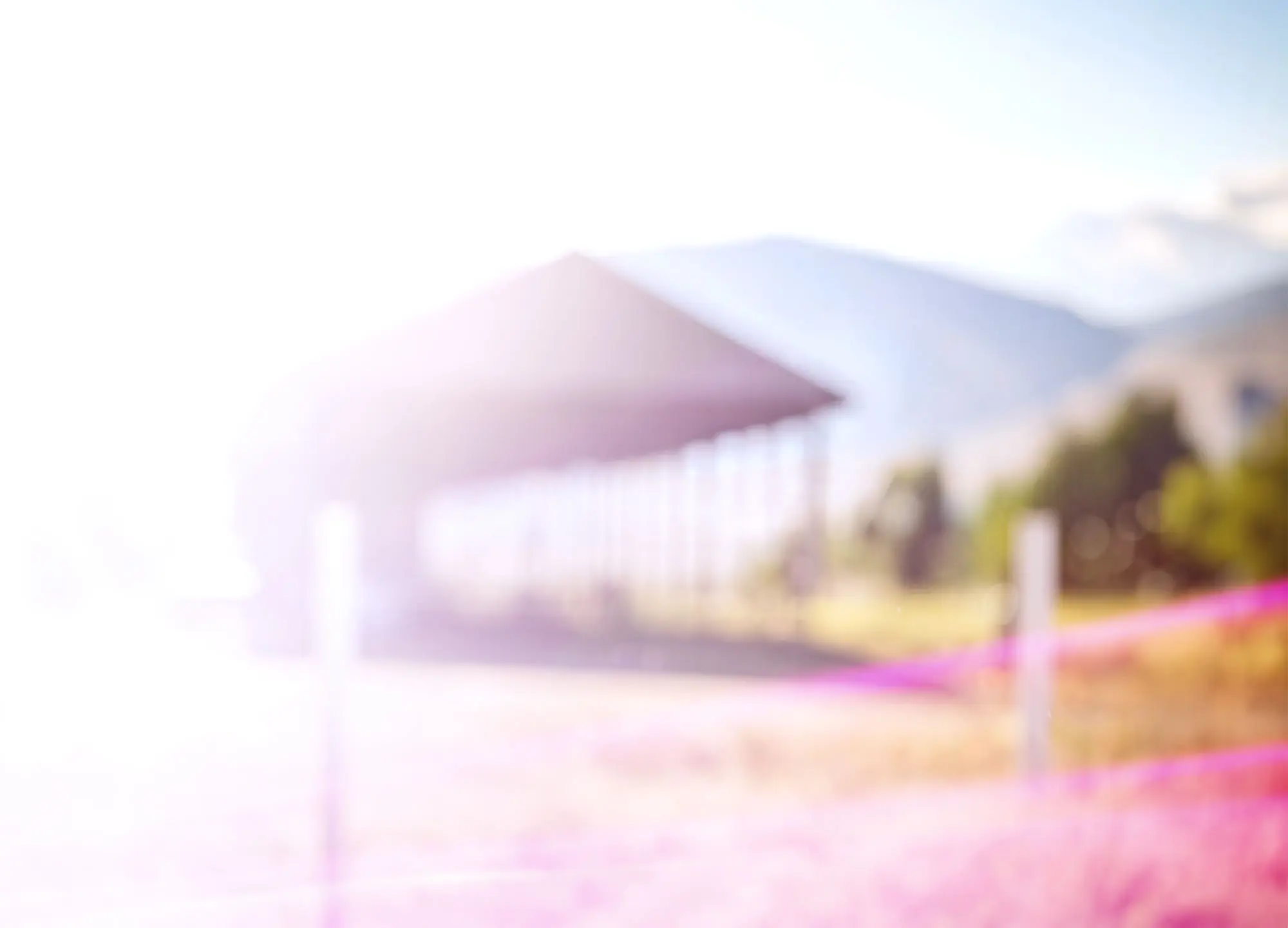 Blurry, bright outdoor image of an open-sided building, distant mountains, and a pink barrier.