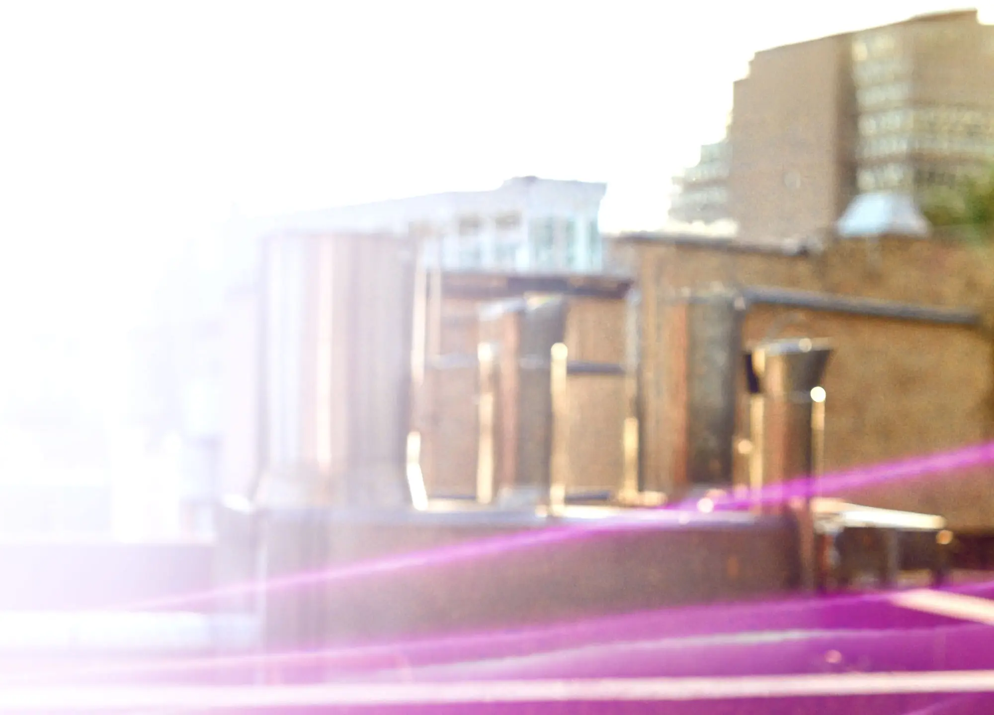 Out-of-focus city buildings and rooftop structures with bright light and purple flares.